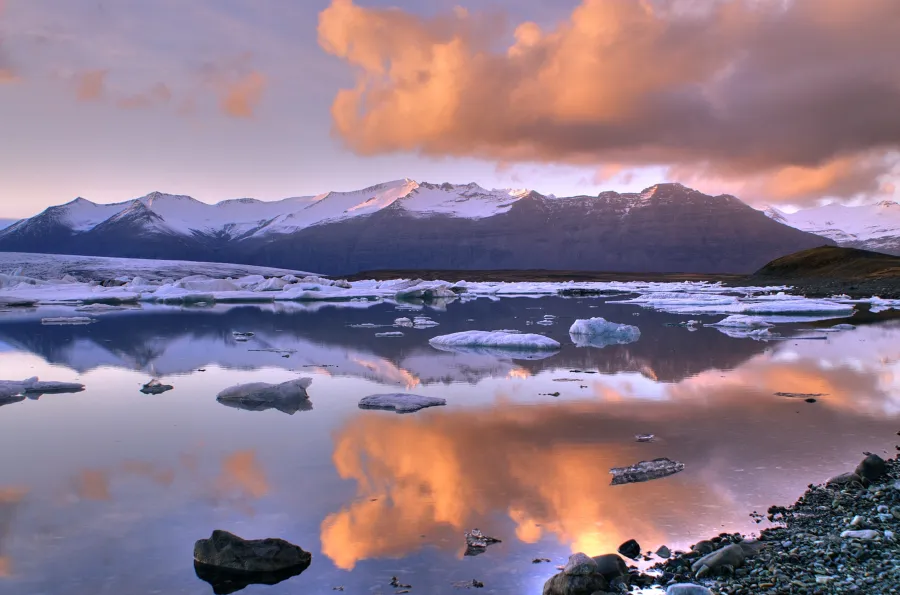 Deep blue glacial ice calving into a grey glacial lagoon under an overcast sky