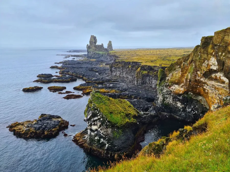 A spectacular view of the rugged basalt cliffs of Reykjanes, Iceland, meeting the ocean under a cloudy sky.